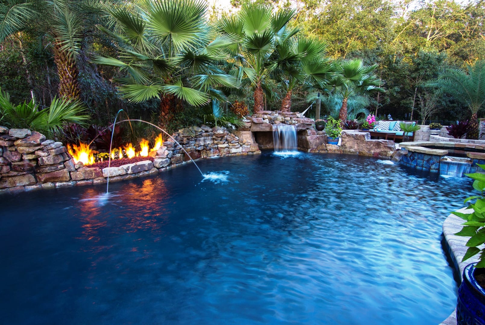 A pool with a waterfall and fire pit.